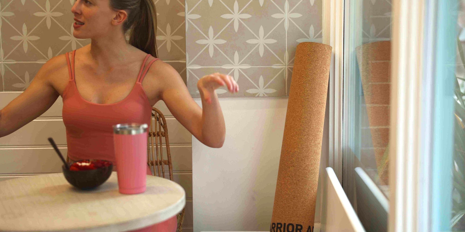 woman in pink activewear clothes sitting in a cafe with cork warrior addict yoga mat