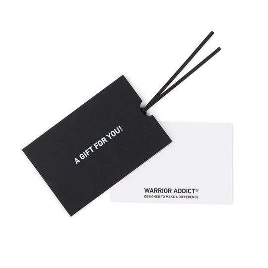 Black gift tag with white text reading "A GIFT FOR YOU!" attached to a white card reading "WARRIOR ADDICT® DESIGNED TO MAKE A DIFFERENCE."