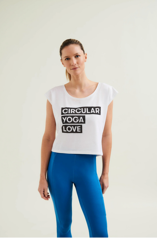 Woman wearing a white tank top with 'Circular Yoga Love' text and blue leggings on a light background