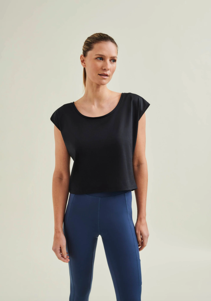 Woman wearing a black top and blue leggings on a plain background