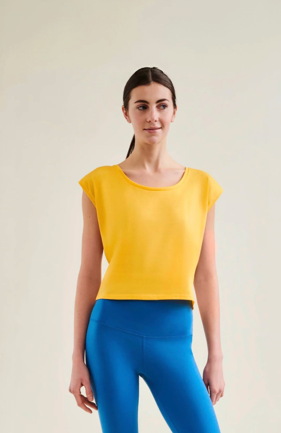 Woman wearing a yellow top and blue leggings against a plain background