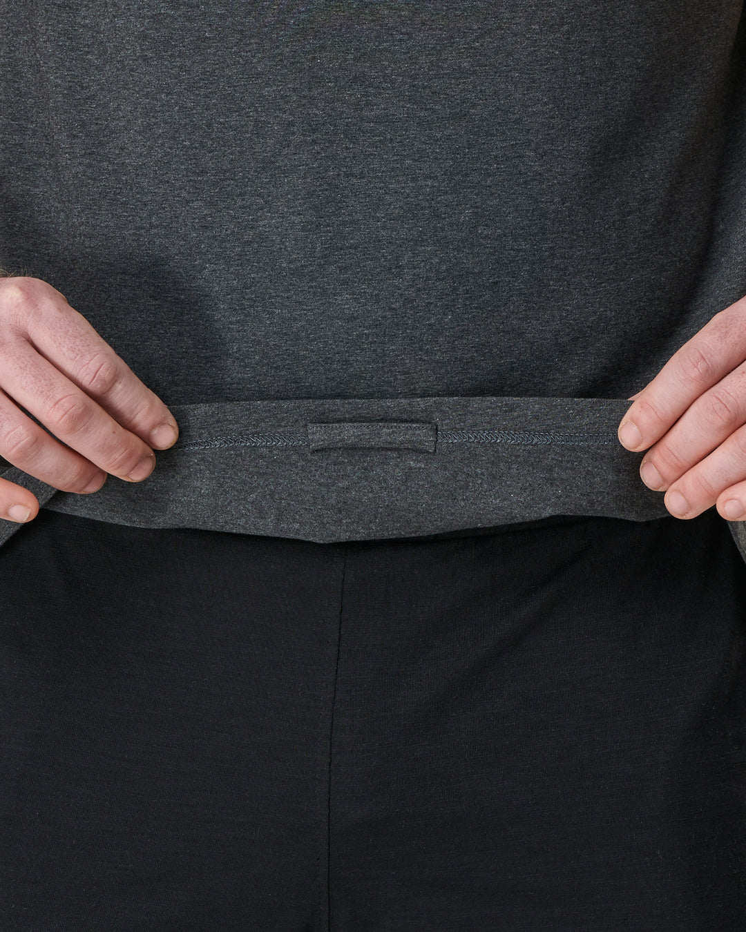 Gray shirt over black pants with hands pulling on the shirt.