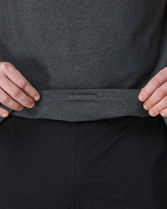 Gray shirt over black pants with hands pulling on the shirt.