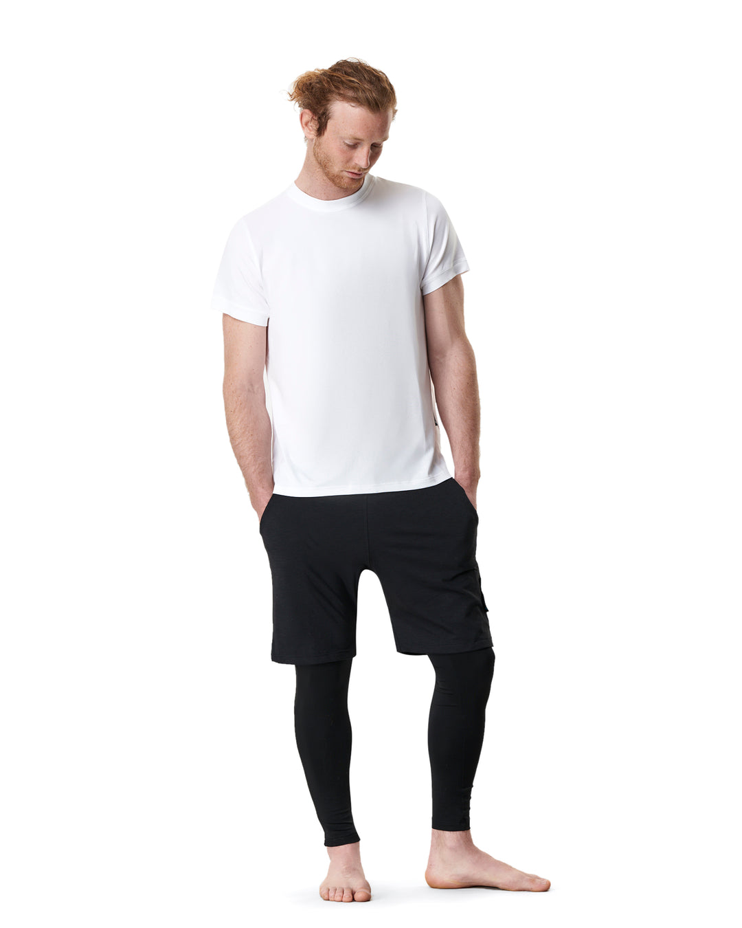 Man in white t-shirt, black shorts over leggings, and barefoot.