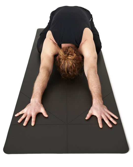 Man in Child's Pose on a black yoga mat.