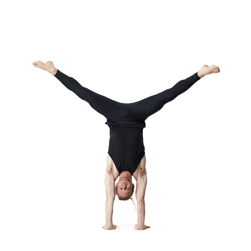 Man in black athletic wear doing a handstand with legs spread.