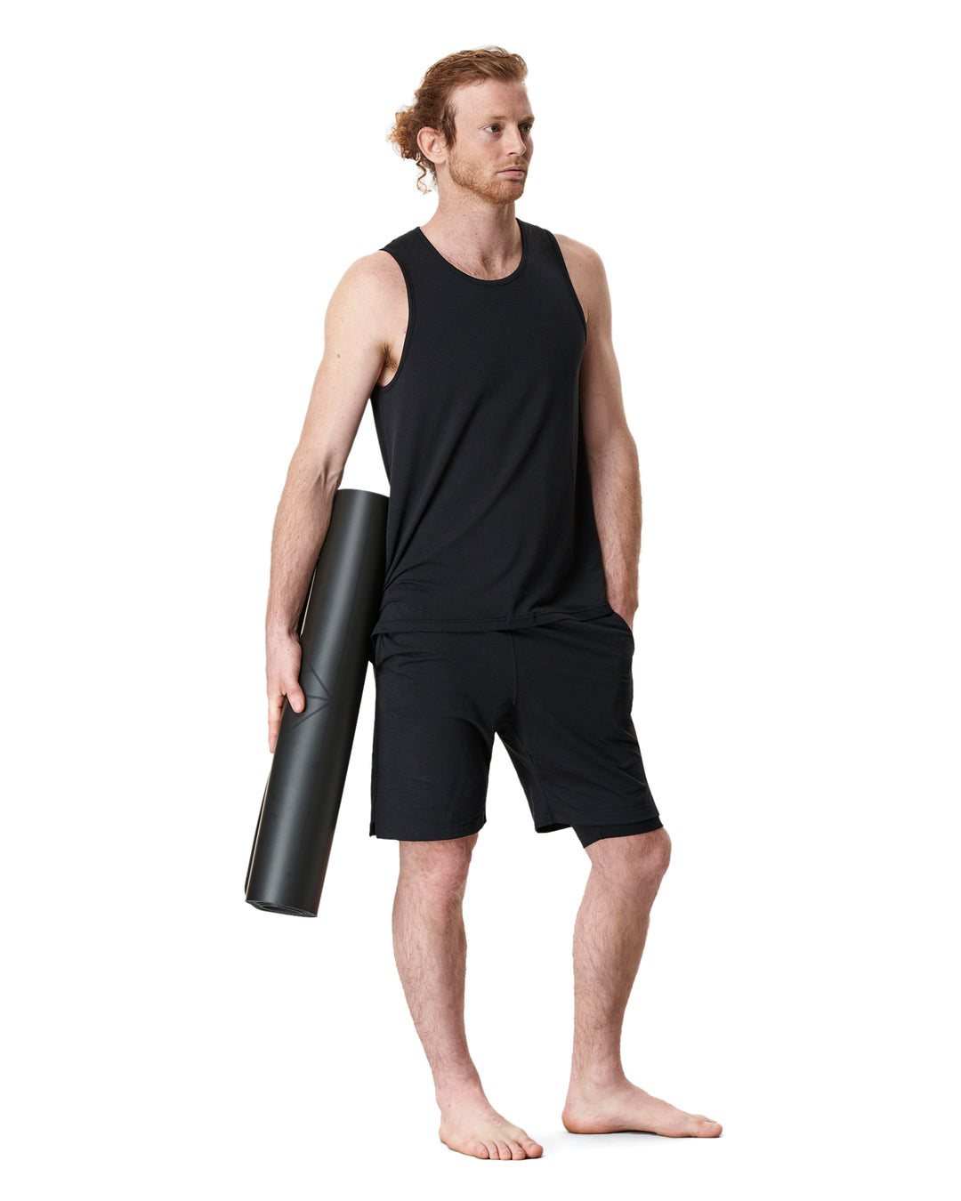 Man holding yoga mat wearing black athletic wear.