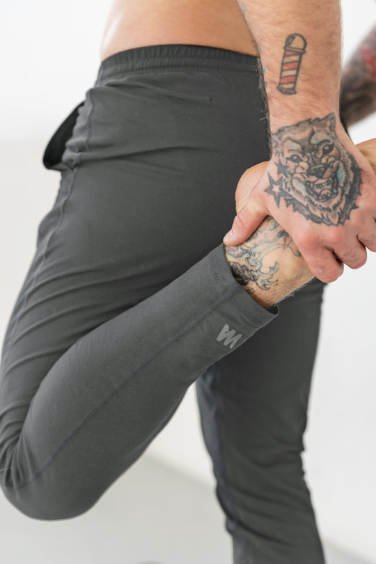 Gray workout pants, tattoos, stretching.