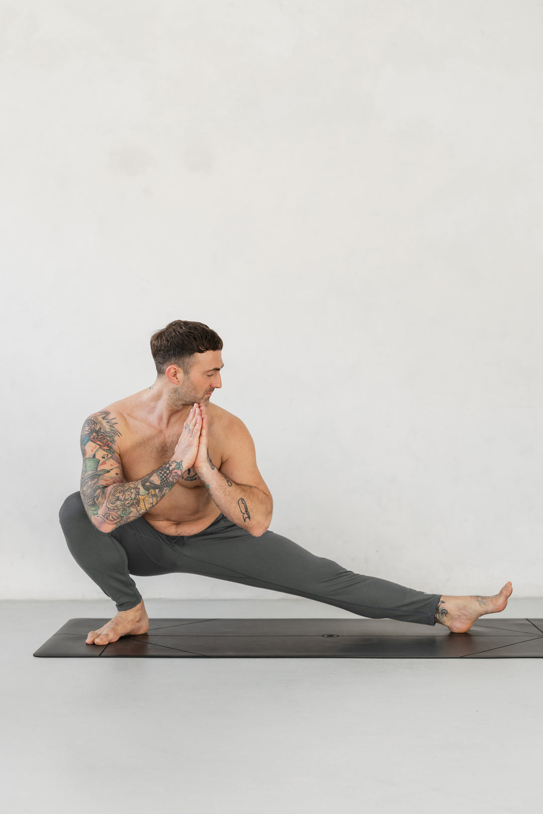 Man in yoga pose on black mat, wearing gray pants.