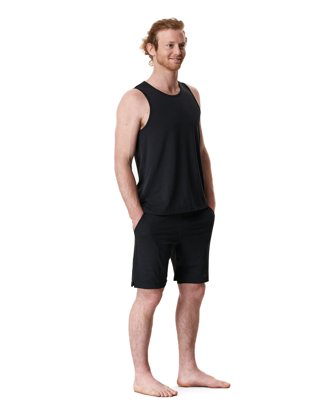 Man in black tank top and shorts, standing with hands in pockets.