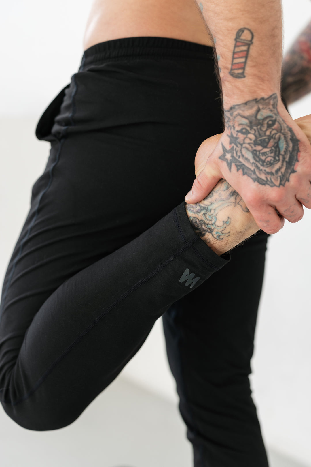 Man stretching, black workout pants, tattoos.