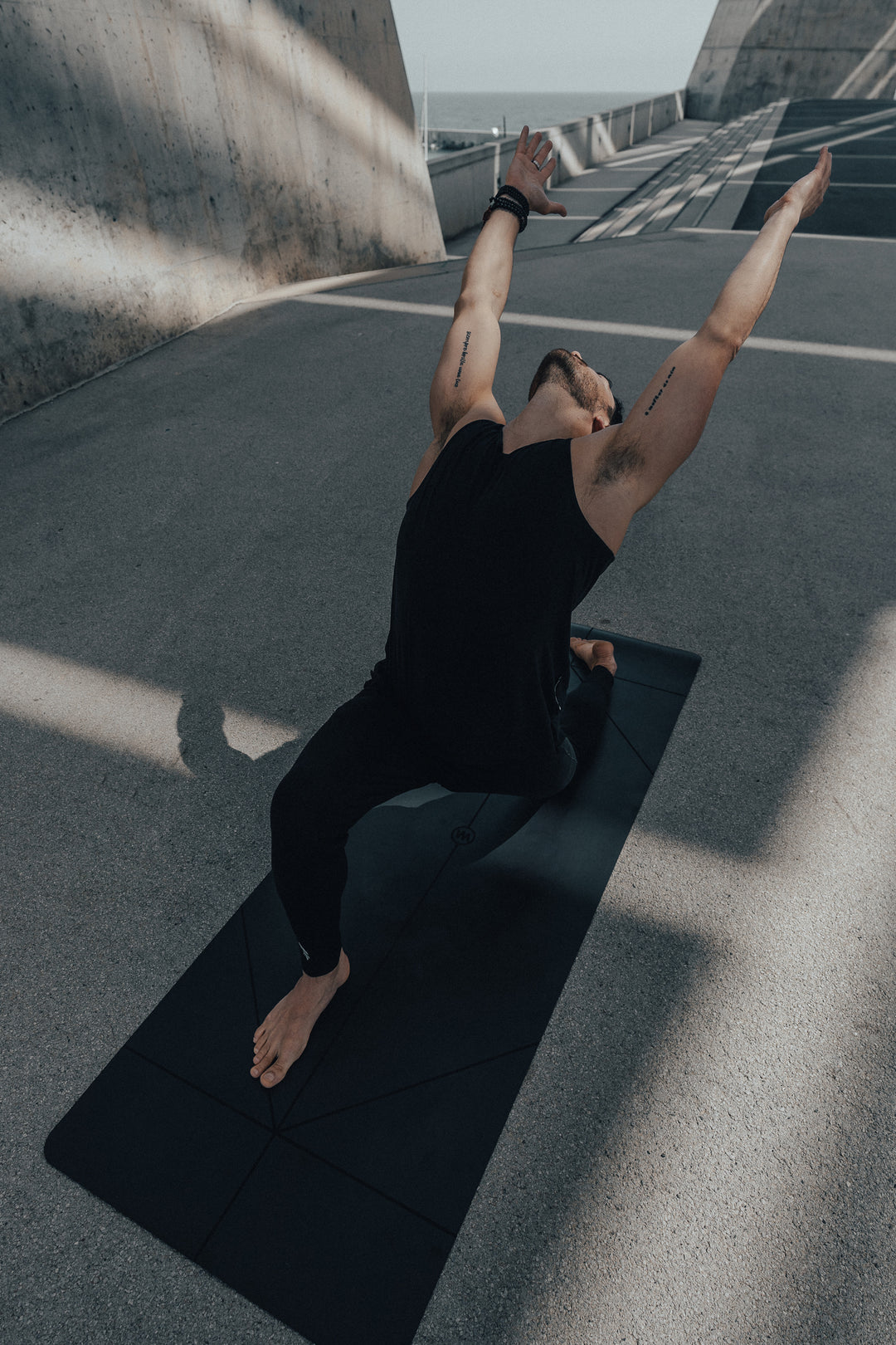 Person practicing yoga on a black Warrior Yoga Mat in an urban setting with concrete walls and a road.