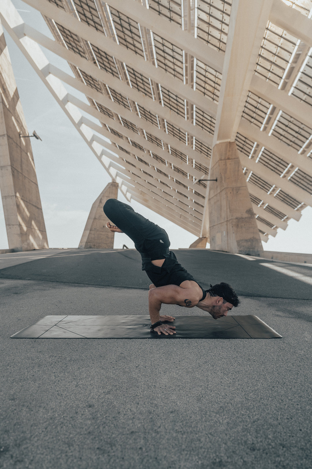 Person doing a handstand on a  black Warrior Yoga Mat under a large architectural structure.