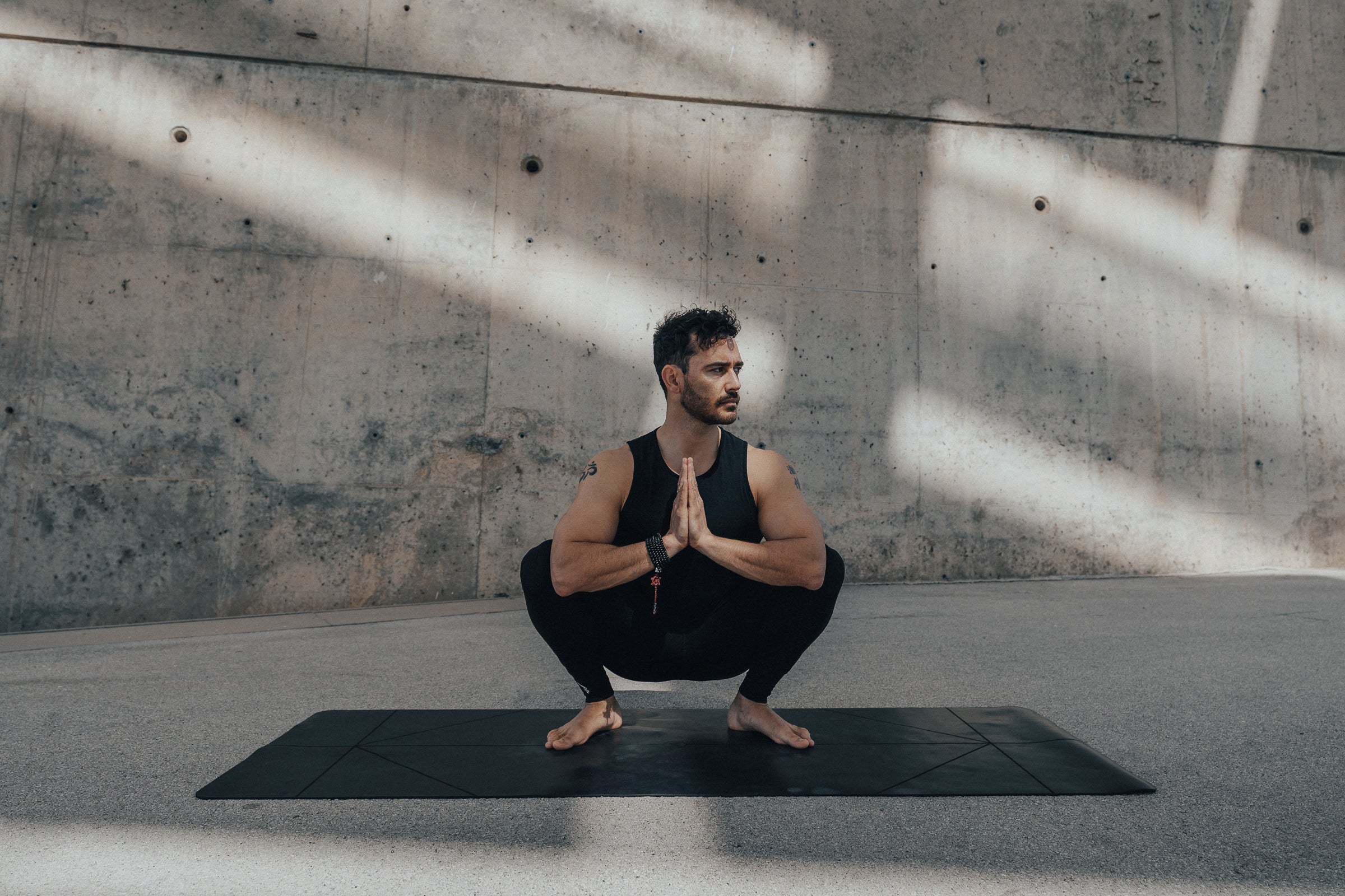 Man in Warrior Addict's  men's activewear doing a  yoga pose on a Warrior Yoga Mat against a concrete wall.