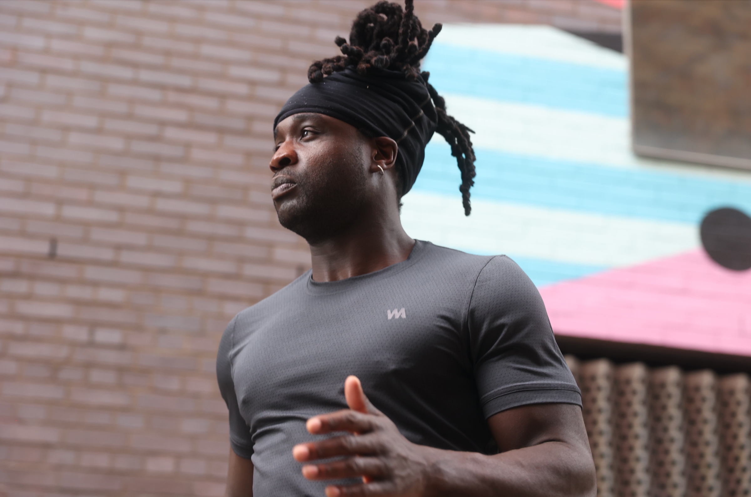 Man wearing Warrior Addicts black  Warrior Skin T-shirt with a logo, standing against a brick wall.