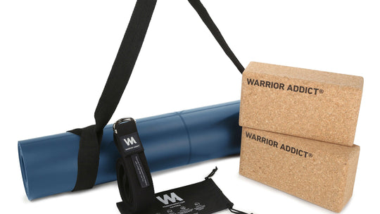 Close-up studio shot of a rolled blue yoga mat in a black carrier, yoga strap, yoga blocks, and a bag for a yoga strap.