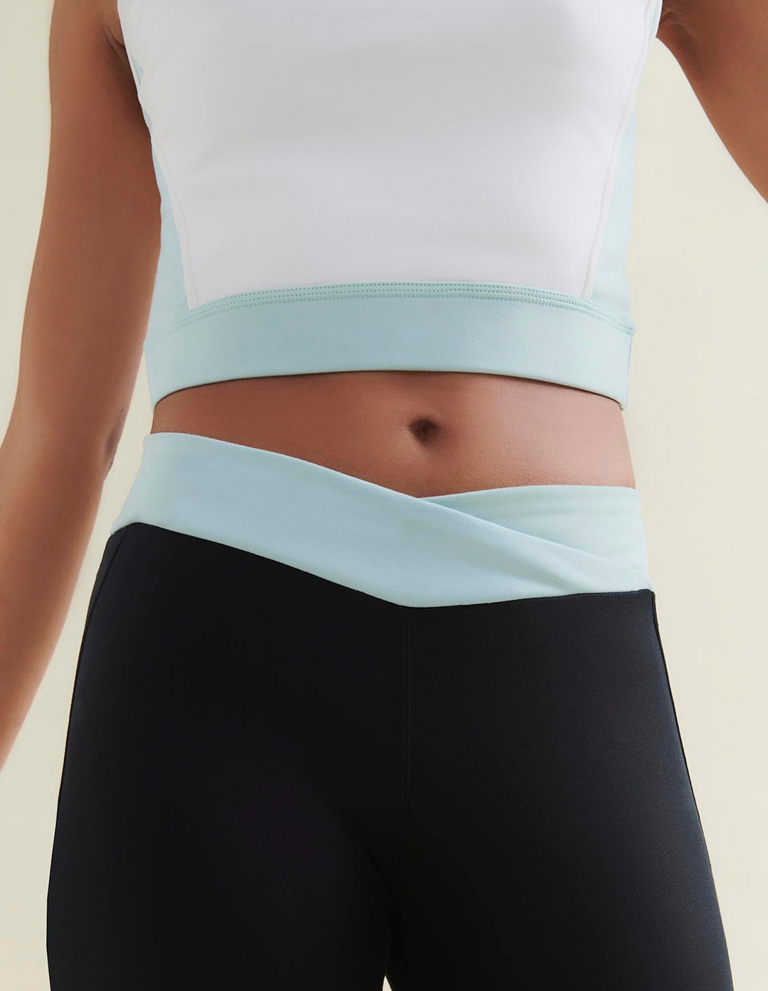 Woman wearing a white crop top and black leggings with light blue waistband on a neutral background