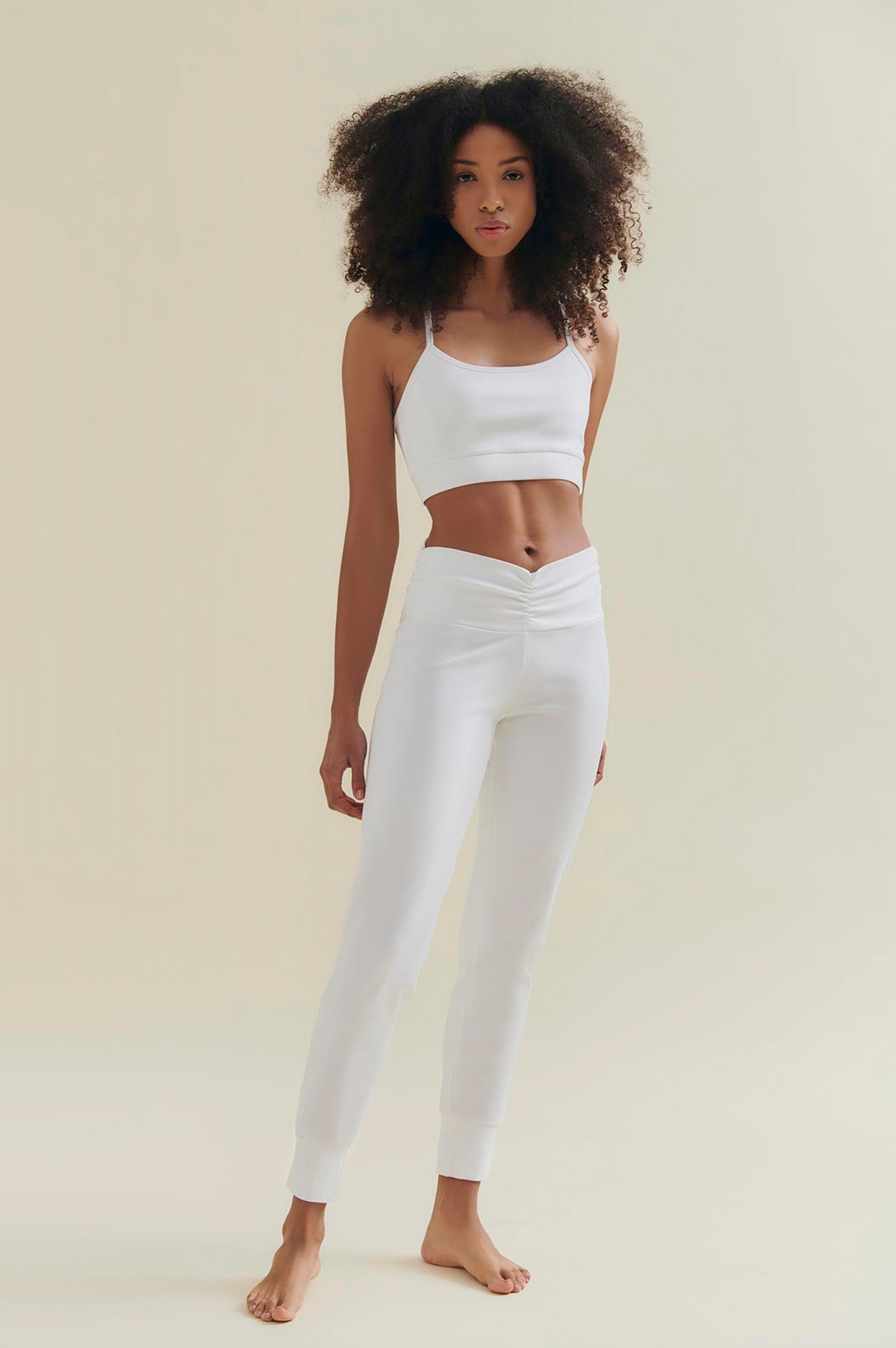 Woman wearing a white tank top and white yoga pants on a beige background