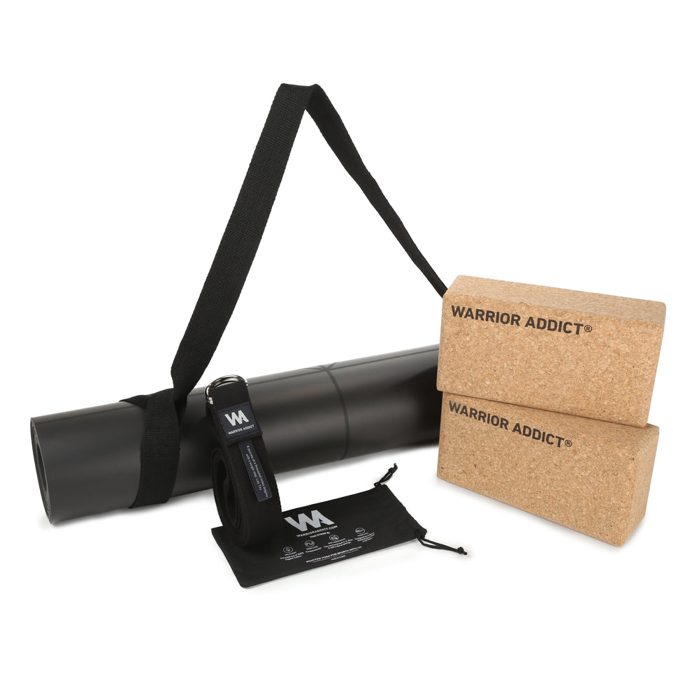 Yoga mat and props including two cork blocks with "Warrior Addict" branding, a black yoga strap, and a carrying bag.