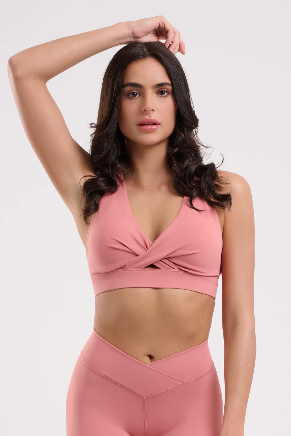 Woman in pink sports bra and leggings, hand on head.