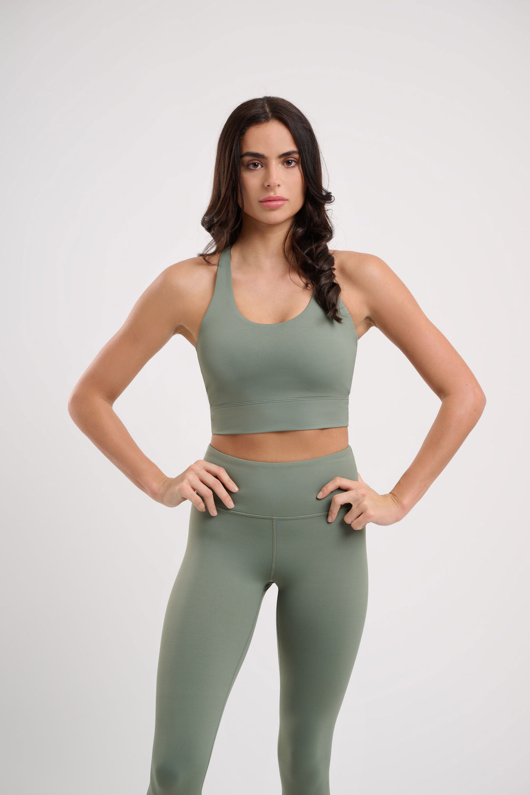 Woman in green sports bra and leggings with hands on hips.