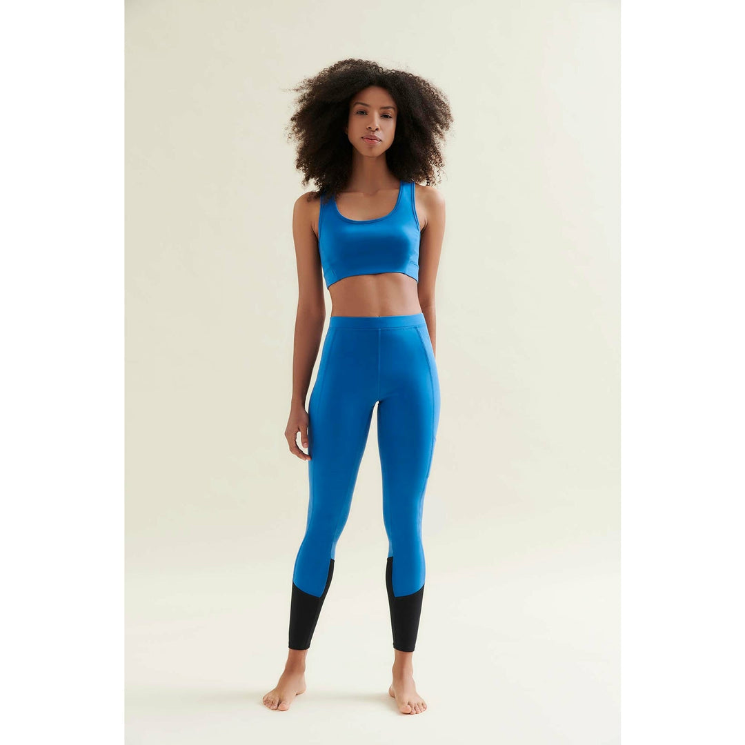 A Black woman poses in a blue sports bra and matching leggings with black accents.