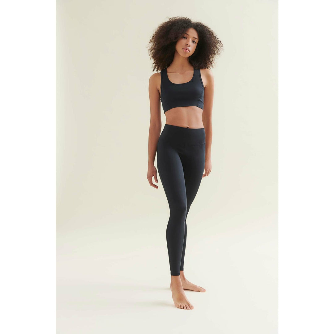 Woman in black sports bra and leggings standing barefoot.
