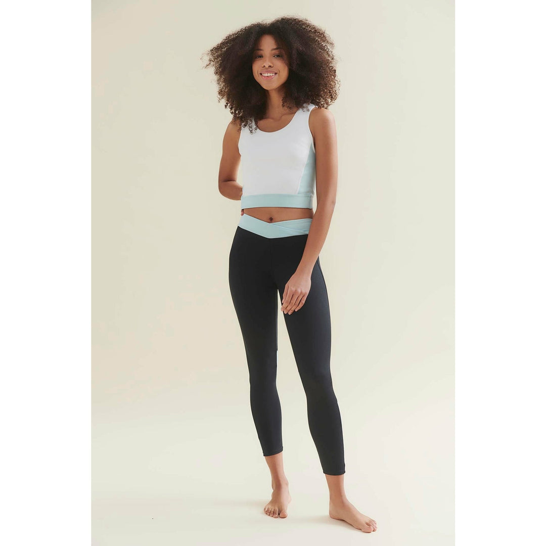 Woman in white and teal crop top with black leggings, barefoot.