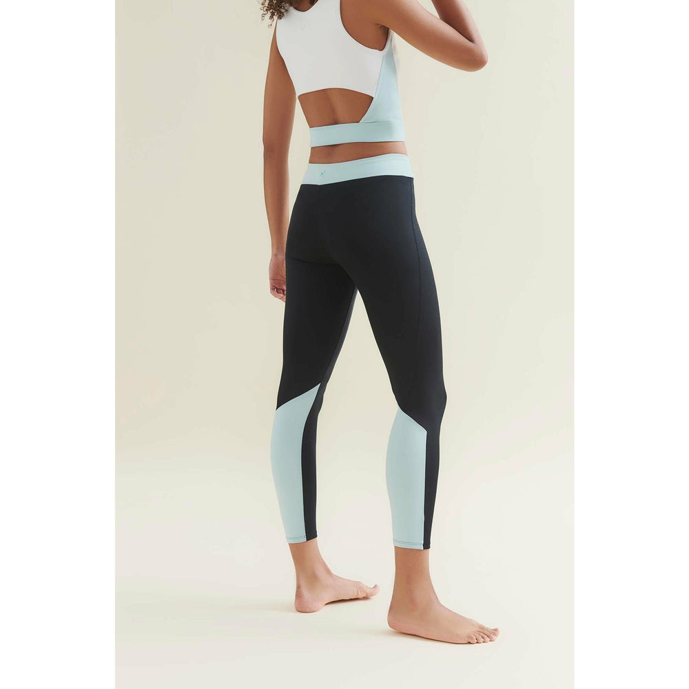 Woman wearing a white and light blue sports bra and black leggings with light blue panels.