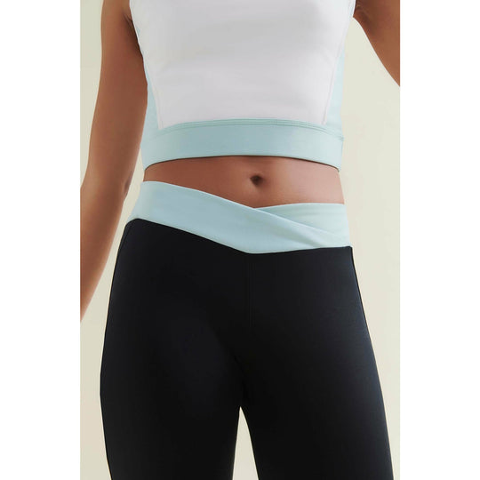 Woman wearing a white and turquoise cropped top and black leggings.