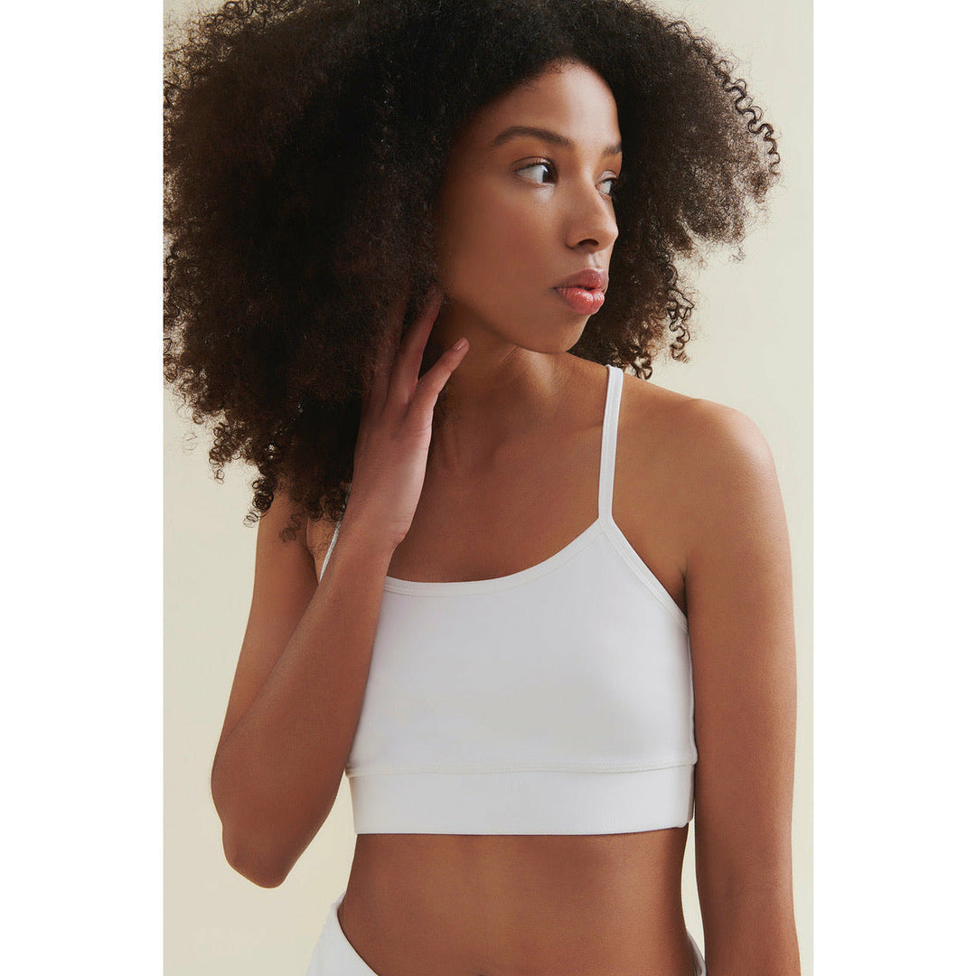 Woman with dark curly hair, wearing a white bra top.