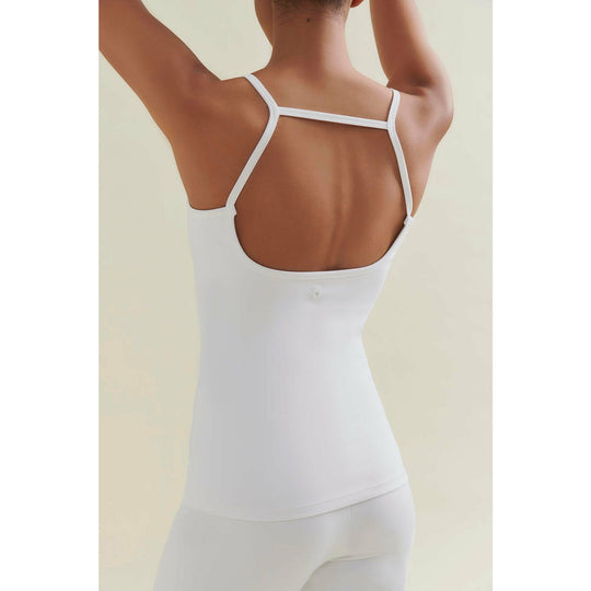 A woman in a white tank top and leggings, with her arms raised.