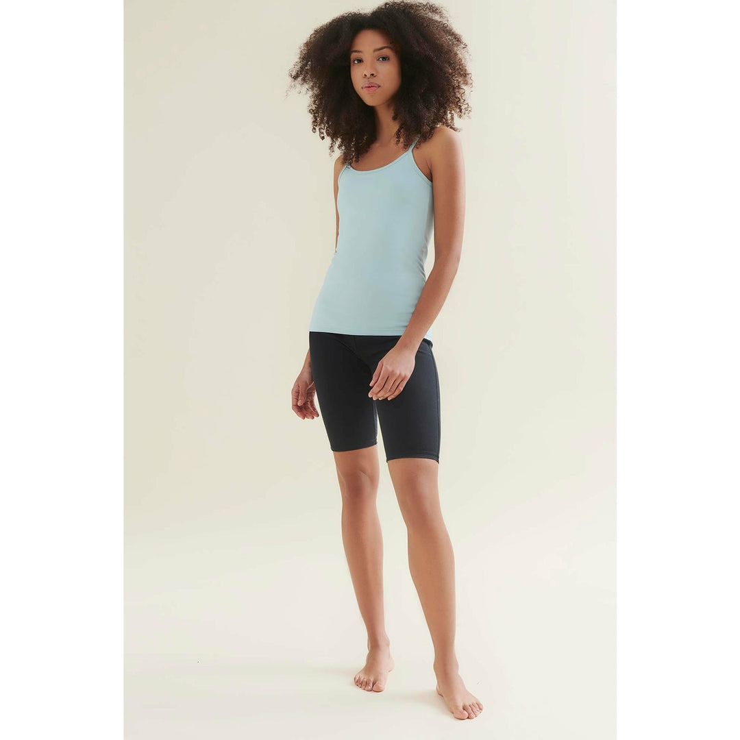 Woman in light blue tank top and black shorts standing barefoot.