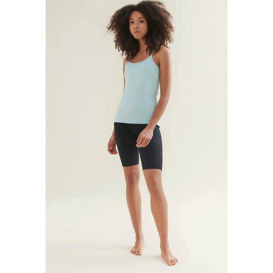 Woman in light blue tank top and black shorts standing barefoot.