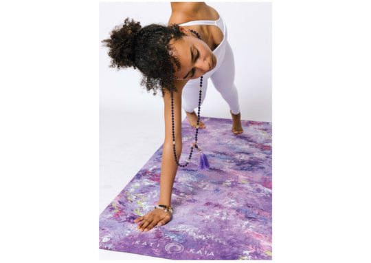 Woman in white doing yoga on a purple painted yoga mat.