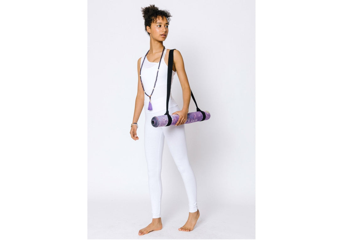 A woman in white yoga clothes holding a purple yoga mat.