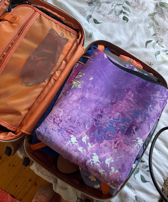 Open suitcase with orange lining and purple patterned garment.