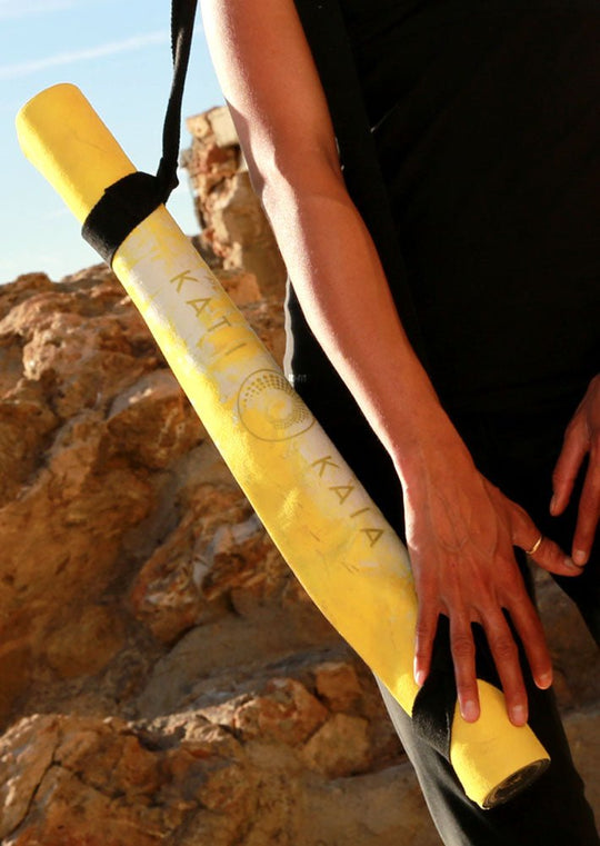Yoga mat strapped to a woman's shoulder, standing in front of rocks.