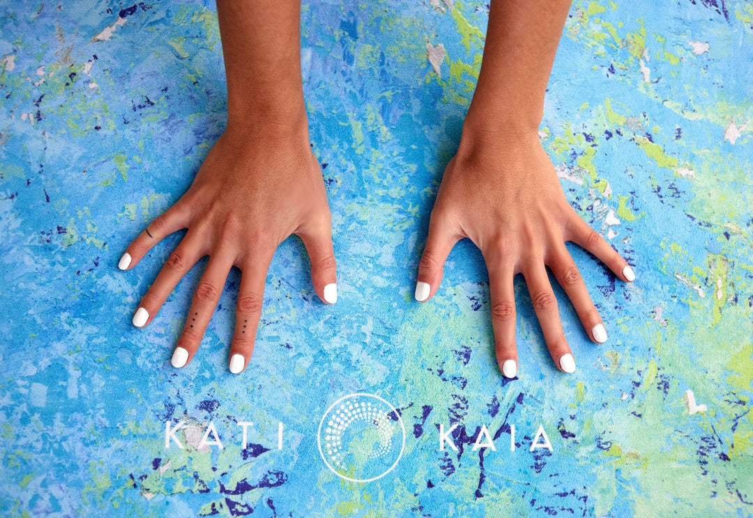 Close-up of two hands with white nails on a patterned yoga mat.