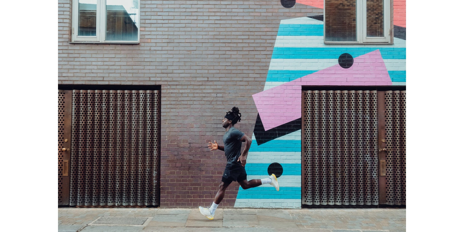 man running in warrior addict running clothes on pavement with mural behind 