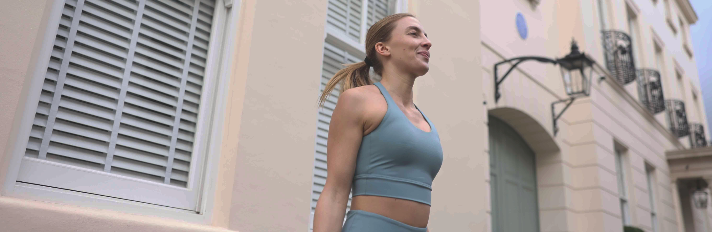 girl in blue yoga top with built in bra standing in front of building