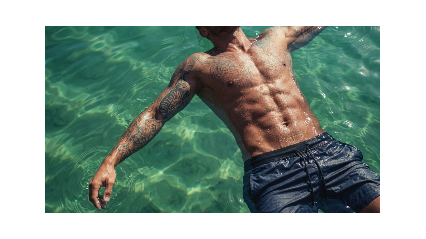 Man with tattoos in clear blue water wearing warrrior addict bodh shorts 