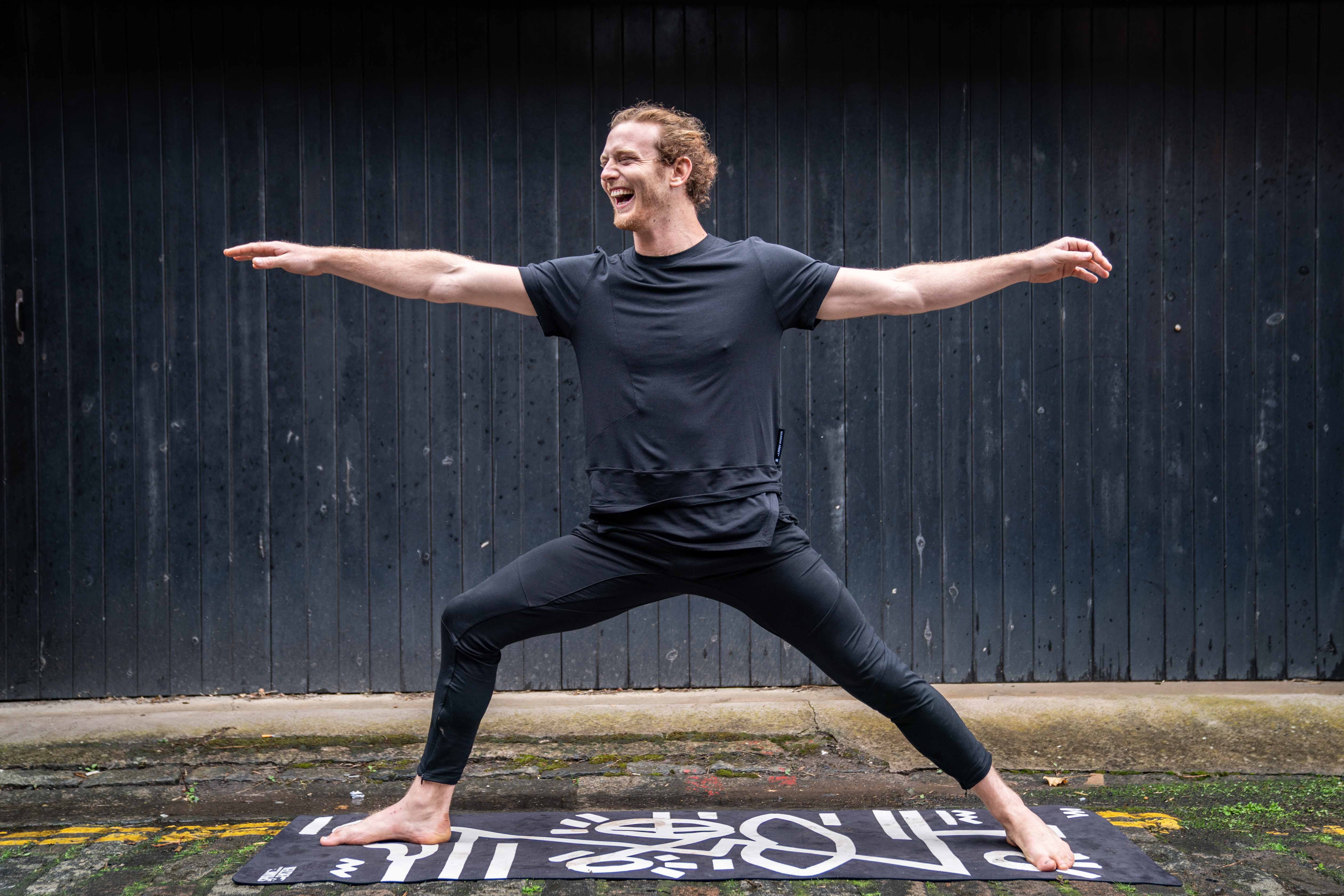 Man in black athletic wear performing a yoga pose on a mat with a dark background