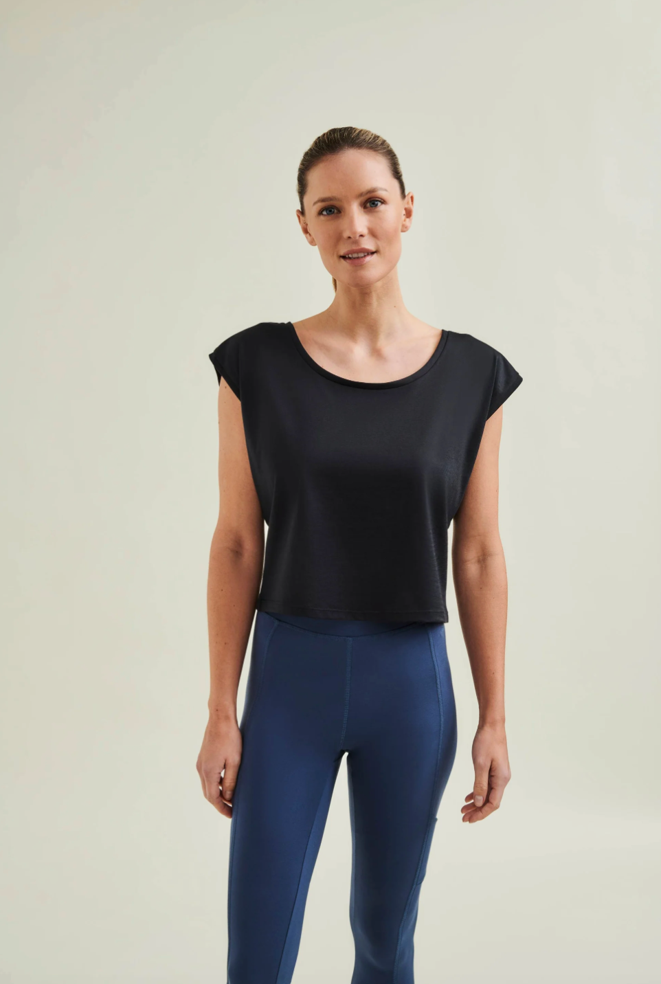 Woman wearing a black top and blue leggings against a plain background