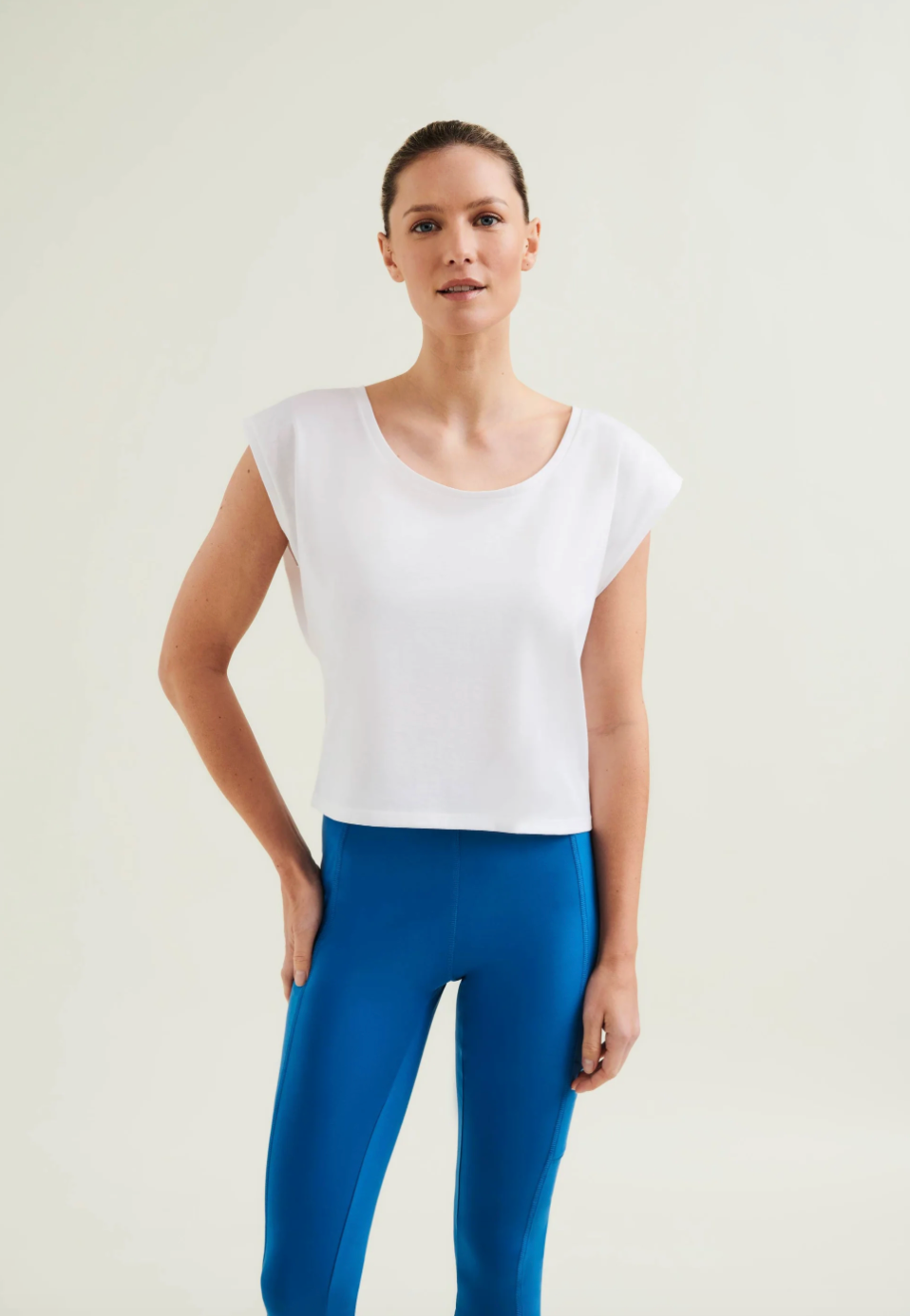 Woman wearing a white top and blue pants on a plain background