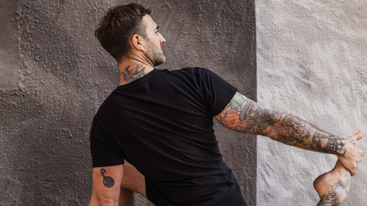 Man wearing black Warrior Addict activewear stretching against a textured wall