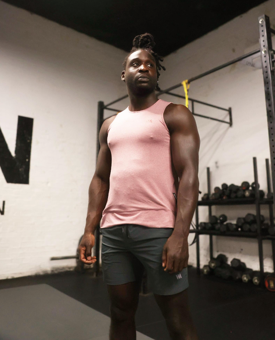 Man wearing a pink  warrior addict tank tank top and gray sports  shorts in a gym setting