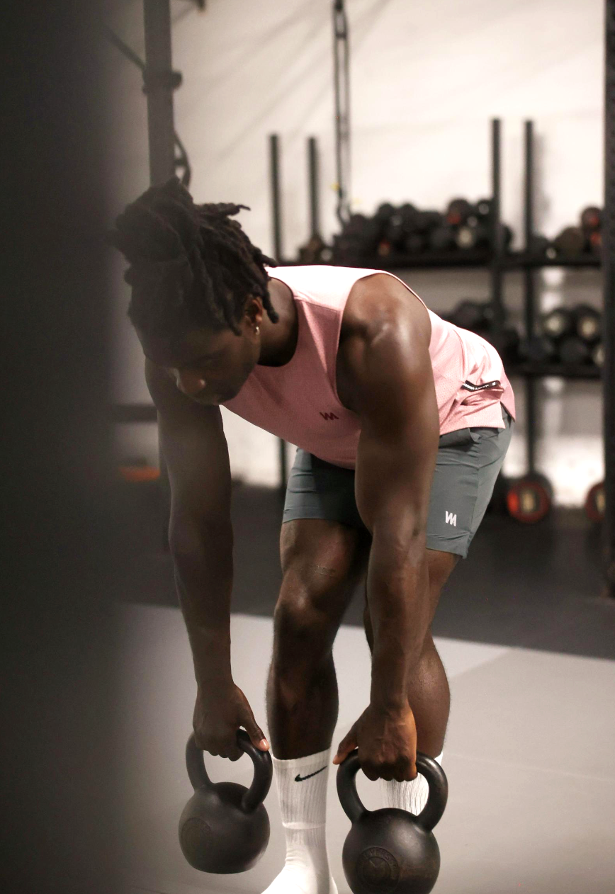 Person lifting kettlebells in a gym setting with warrior addict mens activewear on