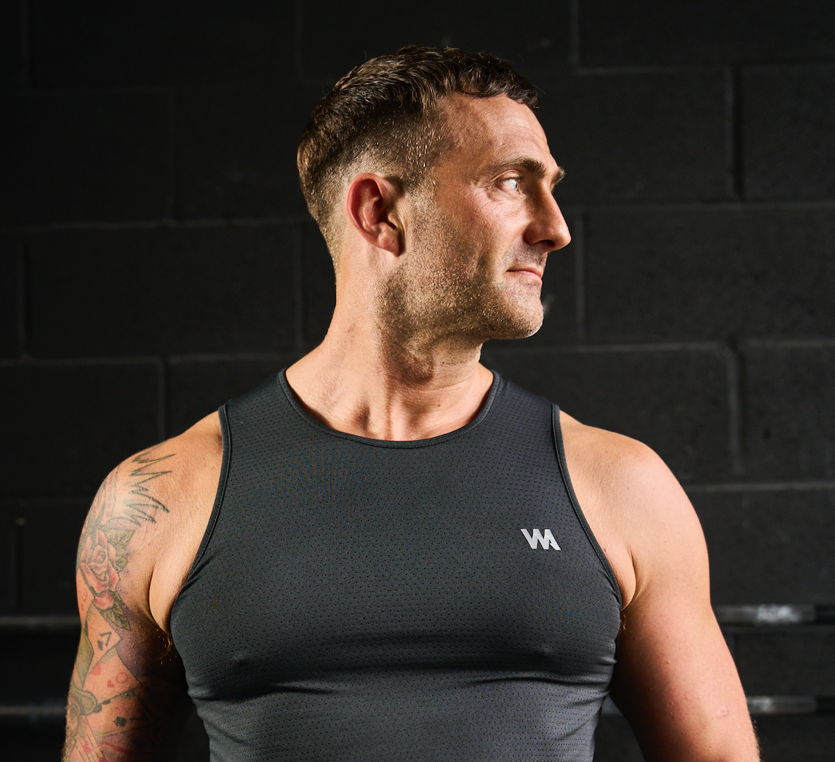 Man wearing a black tank top with a  warrior addict logo on a dark background