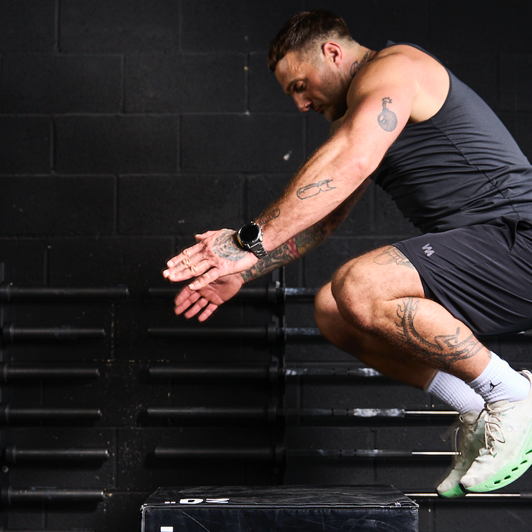 Man performing a squat exercise in a gym setting with black walls and steps.